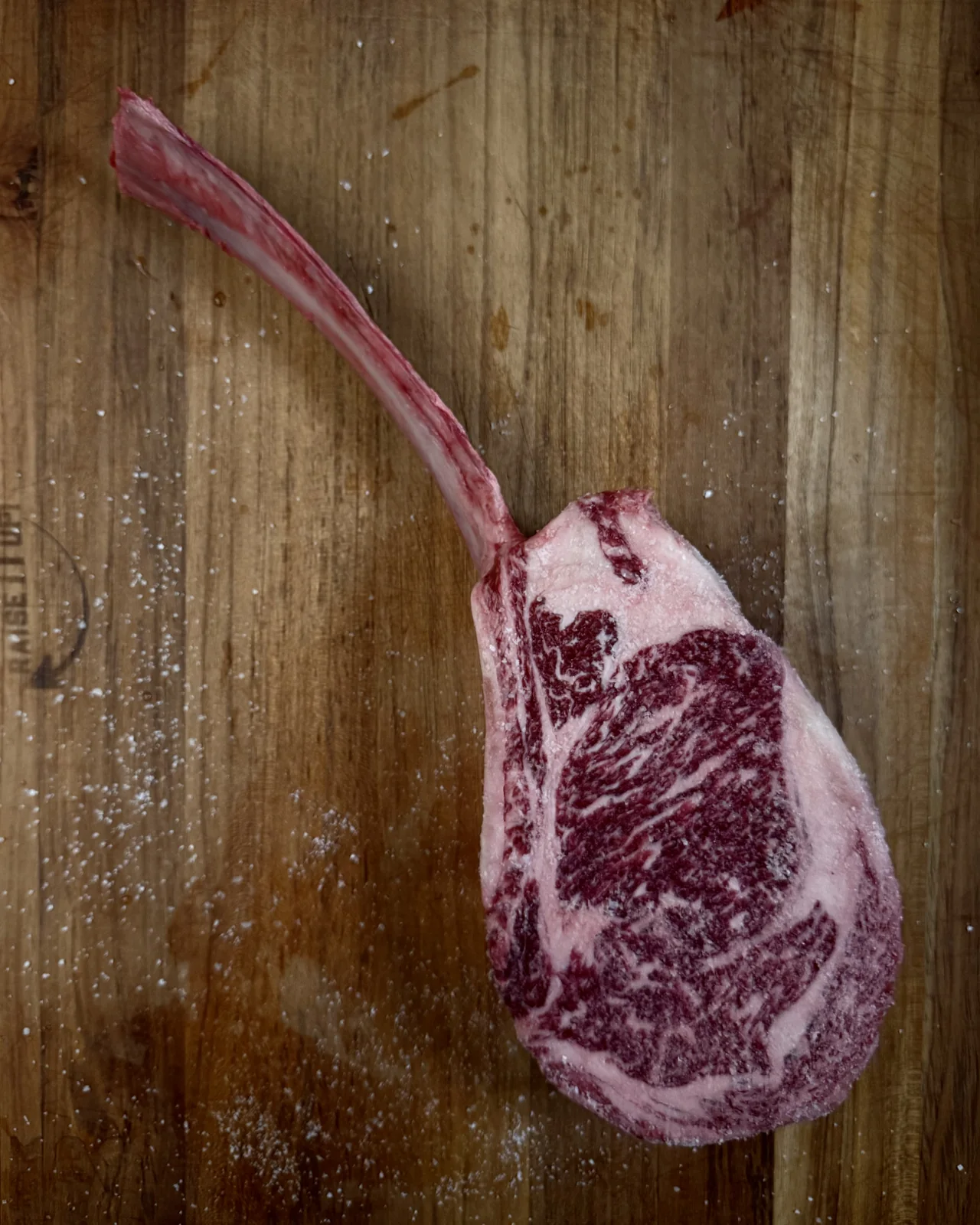 Raw Wagyu tomahawk showing its marbling on a wooden board