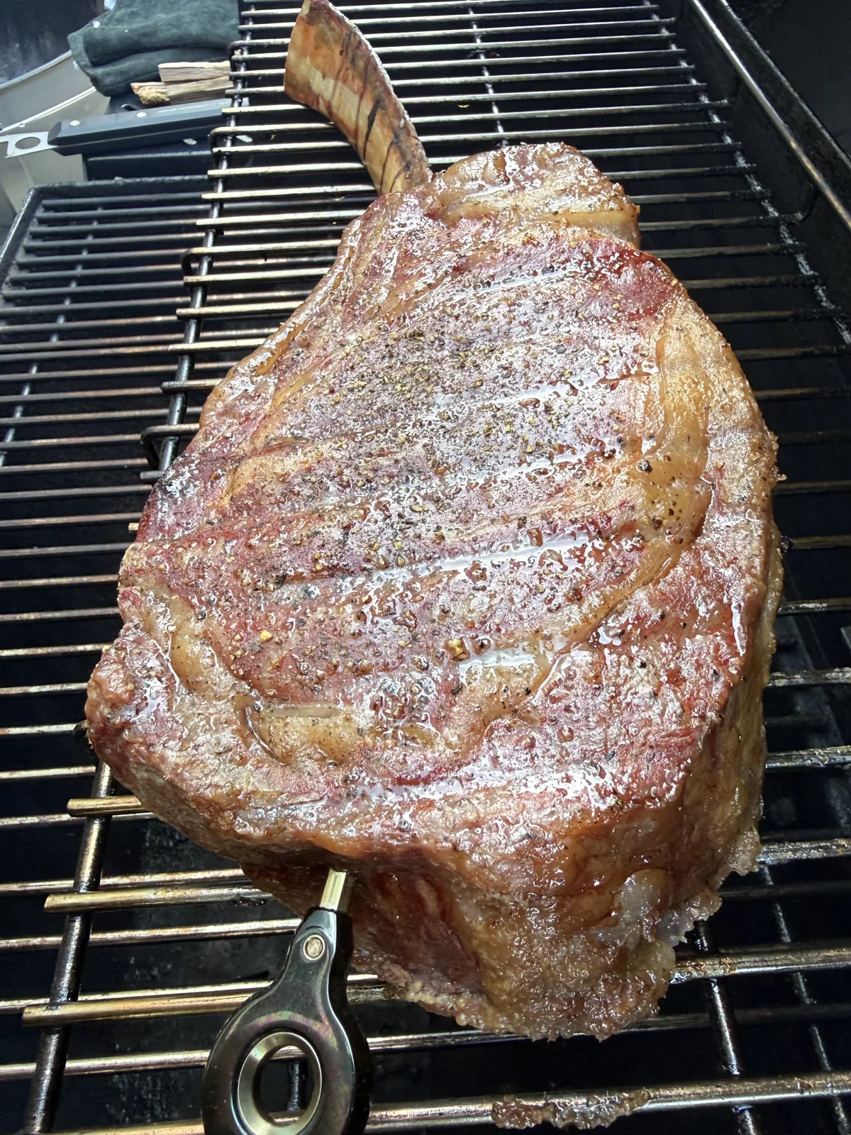 Tomahawk steak browning on the smoker with a temperature probe inserted